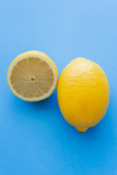 Close up view of cut and whole bright lemons on blue background
