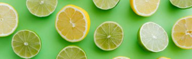 Top view of fresh halves of lemons and limes on green background, banner 