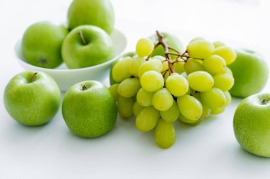 green and ripe apples in bowl near grapes on white