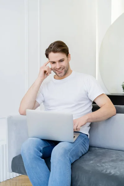 Vrolijk Man Met Behulp Van Laptop Terwijl Zitten Bank Thuis — Stockfoto