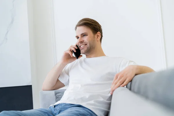 Jovem Alegre Sentado Sofá Embaçado Falando Telefone Móvel — Fotografia de Stock