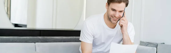 Beyaz Tişörtlü Gülümseyen Adam Kağıda Bakıyor Cep Telefonuyla Konuşuyor — Stok fotoğraf