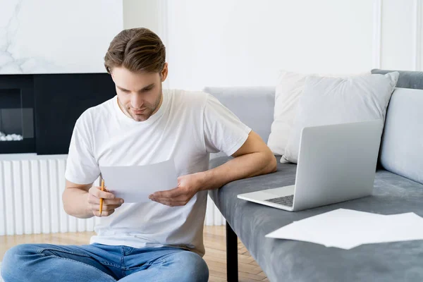 Férfi Nézi Dokumentum Mellett Laptop Papírok Kanapén — Stock Fotó