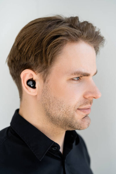 profile of young man listening music in wireless earphone isolated on grey