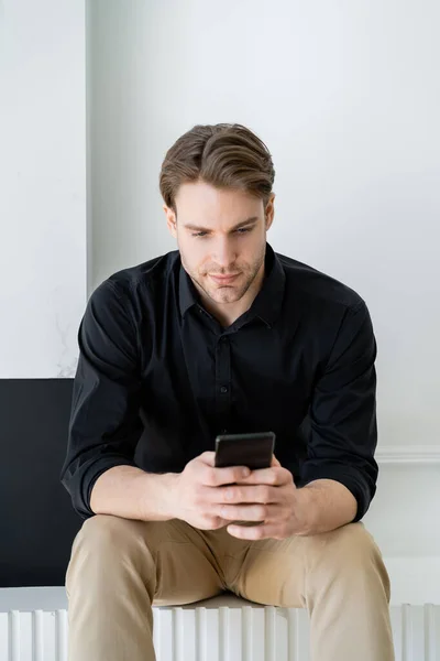 Elegante Uomo Camicia Nera Seduto Casa Messaggistica Smartphone — Foto Stock