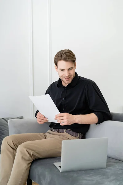 Leende Man Med Dokument Sitter Soffan Och Tittar Laptop — Stockfoto