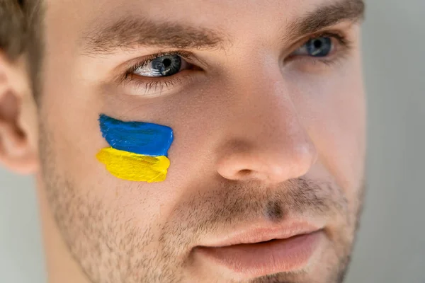 close up portrait of man with ukrainian flag on face isolated on grey