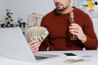 Kumarbazın elinde dolar ve biradan oluşan bulanık dizüstü bilgisayar görüntüsü