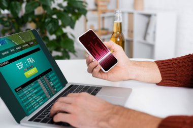 KYIV, UKRAINE - 4 Şubat 2022: spor bahisleri web sitesi olan dizüstü bilgisayarlı akıllı telefon tutan bahisçi görüntüsü