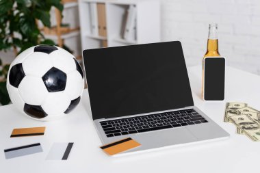 Futbol topunun, kredi kartlarının, dolarların ve bira şişelerinin yanında boş ekranlı bir laptop.