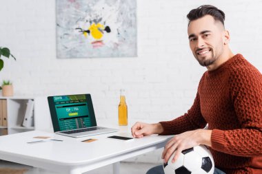 KYIV, UKRAINE - 4 Şubat 2022: Futbol topuyla mutlu bahisçi spor sitesi web sitesi ile dizüstü bilgisayara bakıyor