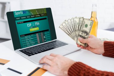 KYIV, UKRAINE - FEBRUARY 4, 2022: partial view of bookmaker with dollars near laptop with sportsbet website 