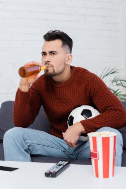 focused football fan drinking beer while watching game on tv at home