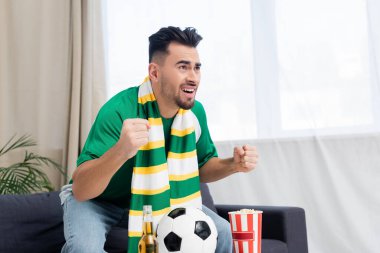 Yumruklarını sıkmış gergin bir adam TV 'de patlamış mısır ve biranın yanında futbol maçı izliyor.