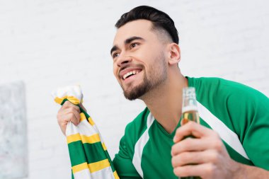 Çizgili atkısı ve bira izleyip evinde maç izleyen neşeli bir spor taraftarı.