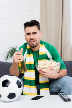 Futbol topunun yanındaki TV 'de patlamış mısır ve bira izleyip canı sıkkın spor fanatiği