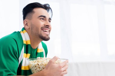 Neşeli spor fanatiği evde patlamış mısır seyrediyor.