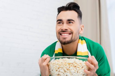 thrilled sports fan holding bowl of popcorn while watching championship at home clipart