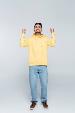 full length of cheerful bookmaker showing triumph gesture and looking up on grey