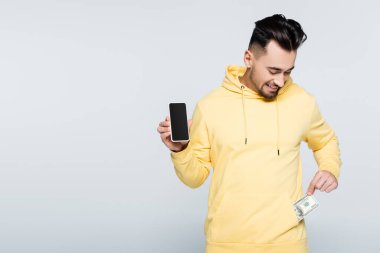 smiling bookmaker with mobile phone taking money from pocket isolated on grey
