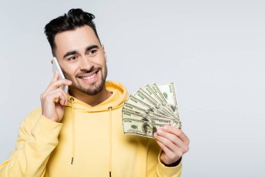 pleased gambler talking on mobile phone and holding dollars isolated on grey