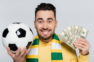 excited gambler with dollars and soccer ball looking at camera isolated on grey