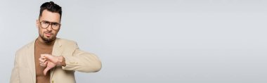 dissatisfied critic showing thumb down while looking at camera isolated on grey, banner