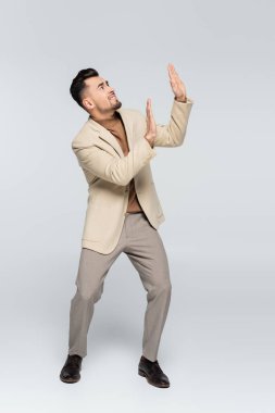 full length of worried critic looking up and showing stop gesture on grey