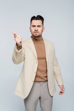 irritated critic looking at camera and pointing with finger isolated on grey