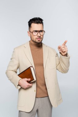 serious literary critic holding book and pointing with finger isolated on grey