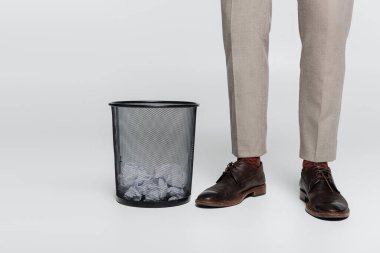 partial view of critic standing near trash can with crumpled paper on grey