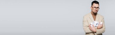 sad critic holding crumpled paper and looking at camera isolated on grey, banner