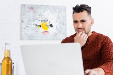 Bulanık bira şişesinin yanındaki dizüstü bilgisayara bakan endişeli bahisçi.