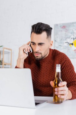 Elinde bira şişesi olan ciddi bir bahisçi bilgisayarın yanında akıllı telefondan konuşuyor.
