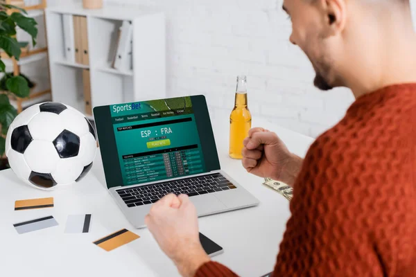 KYIV, UKRAINE - 4 Şubat 2022: Sports sbet web sitesi ile birlikte kredi kartları ve dizüstü bilgisayarın yanında şans için yumruklarını sıkan bulanık kumarbaz