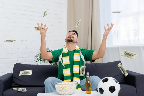 excited bookmaker throwing up money near soccer ball, beer and popcorn