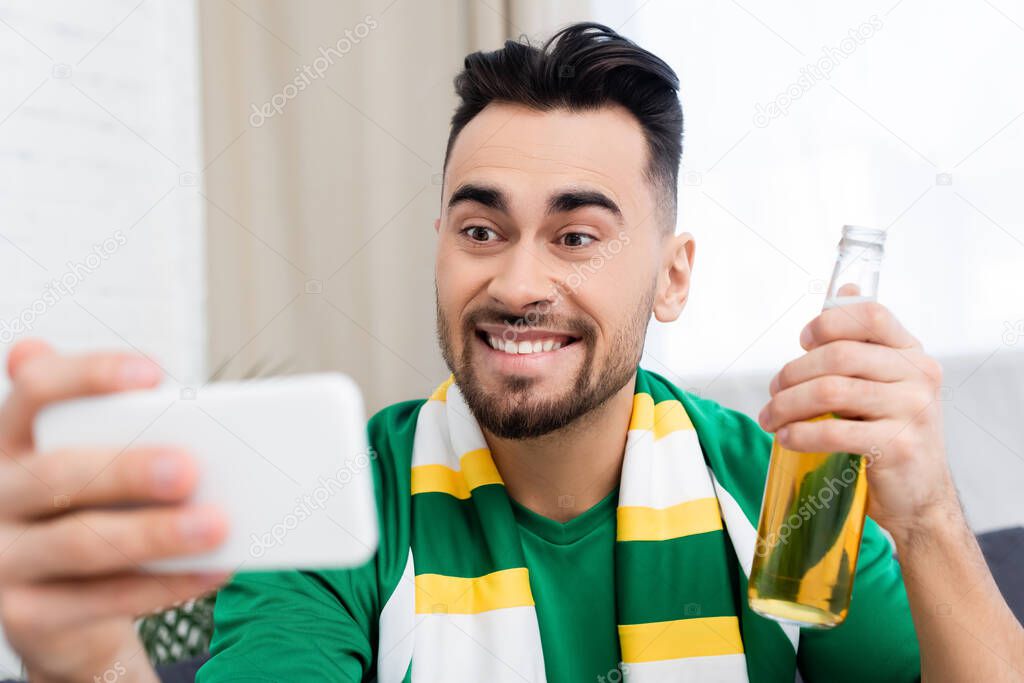 excited sports fan with bottle of beer taking selfie on blurred smartphone
