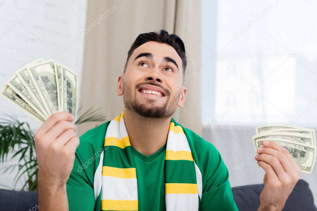 Happy gambler looking up while holding dollars and bottle of beer