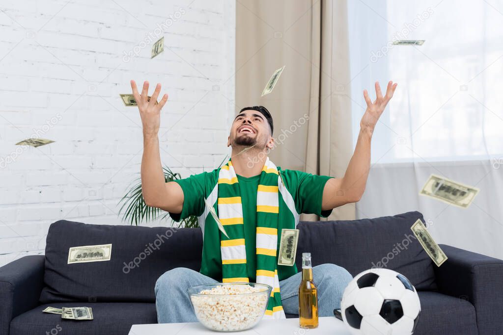 Excited bookmaker throwing up money near soccer ball, beer and popcorn