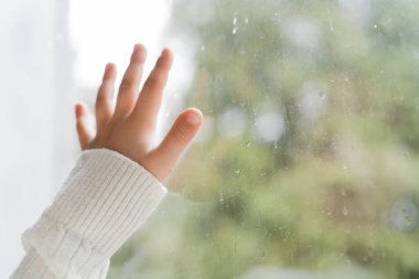 Yağmur damlalarıyla pencerenin yanındaki çocuğun kırpılmış görüntüsü