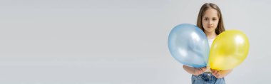 çocuk kameraya bakarken mavi ve sarı balonları gri pankartta izole ediyor.