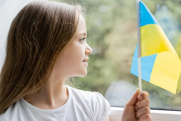 Улыбающаяся Девушка Маленьким Украинским Флагом Смотрящая Окно Дома — стоковое фото