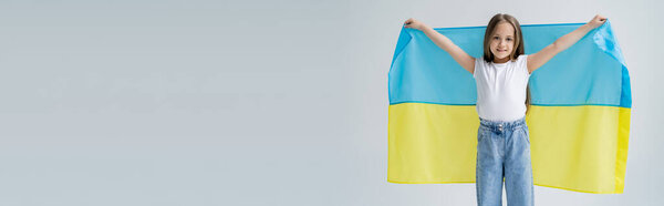 радостная патриотическая девушка с украинским флагом, улыбающаяся в камеру, изолированную на сером, баннер