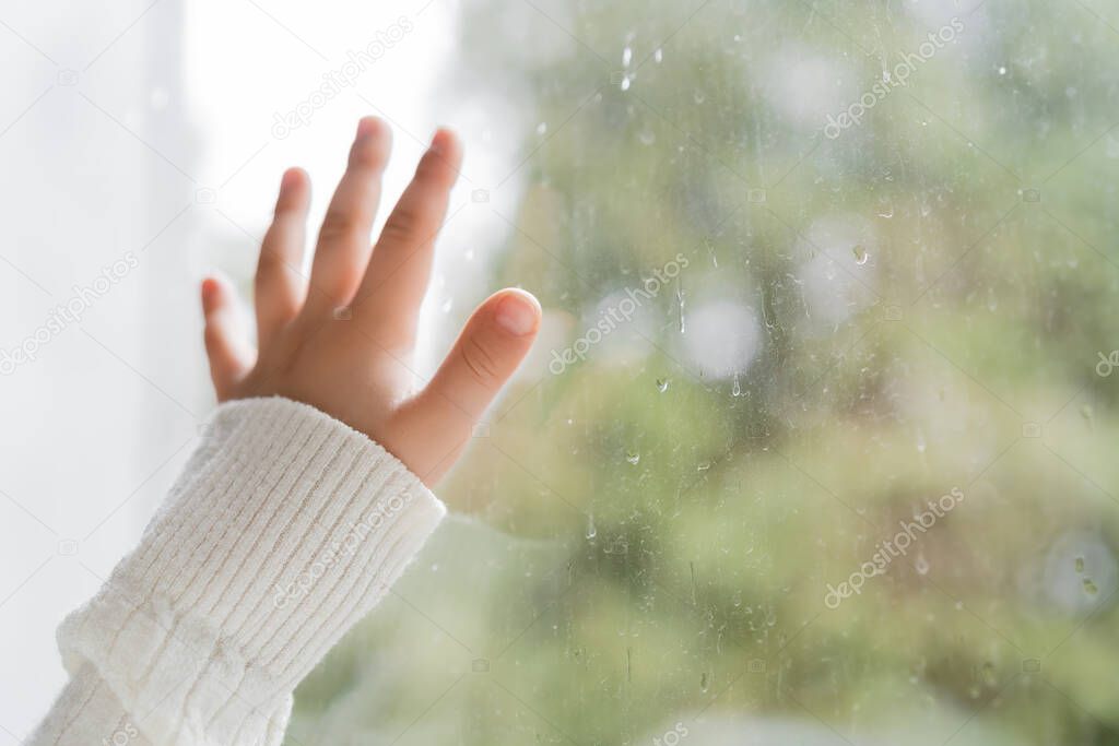 cropped view of hand of child near window with raindrops