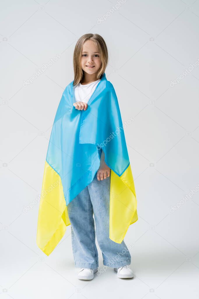 full length view of positive girl covered with ukrainian flag on grey