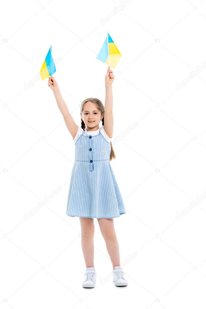 full length view of girl standing with ukrainian flags in raised hands on white