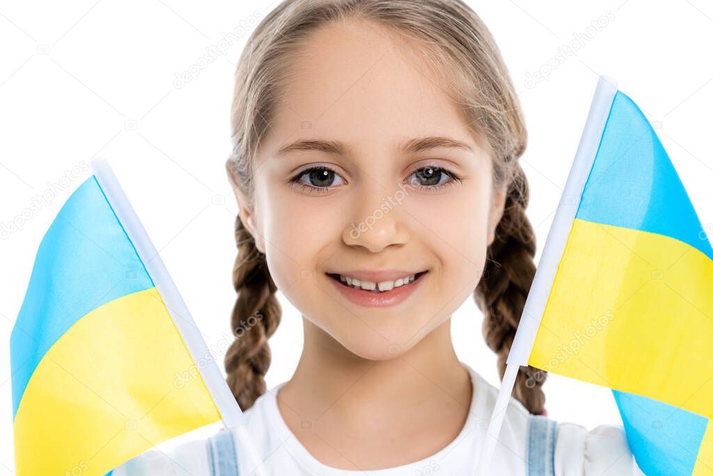 portrait of smiling patriotic girl near ukrainian flags isolated on white