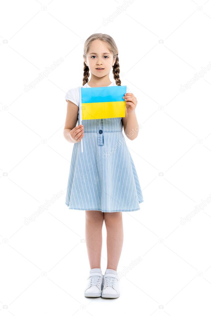 full length view of girl in blue dress holding small ukrainian flag on white