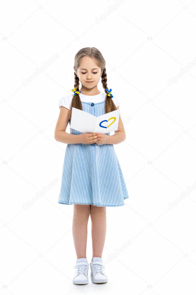 full length view of girl reading postcard with blue and yellow heart on white