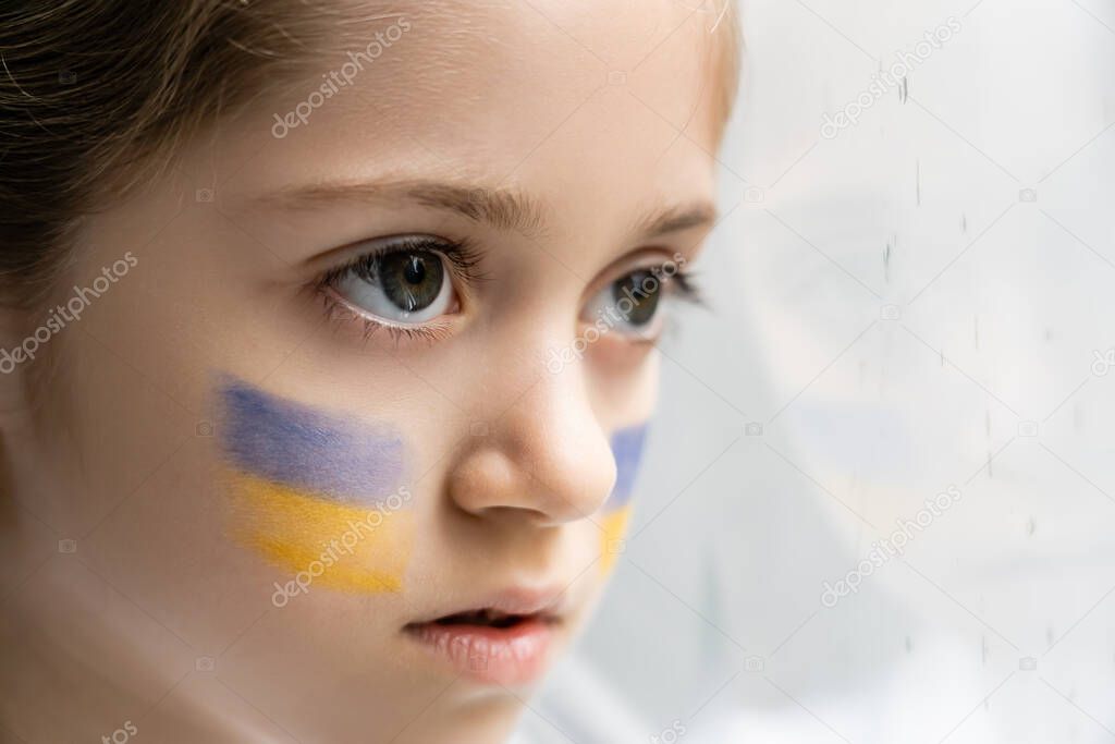 close up portrait of ukrainian child with national flags on face on white background